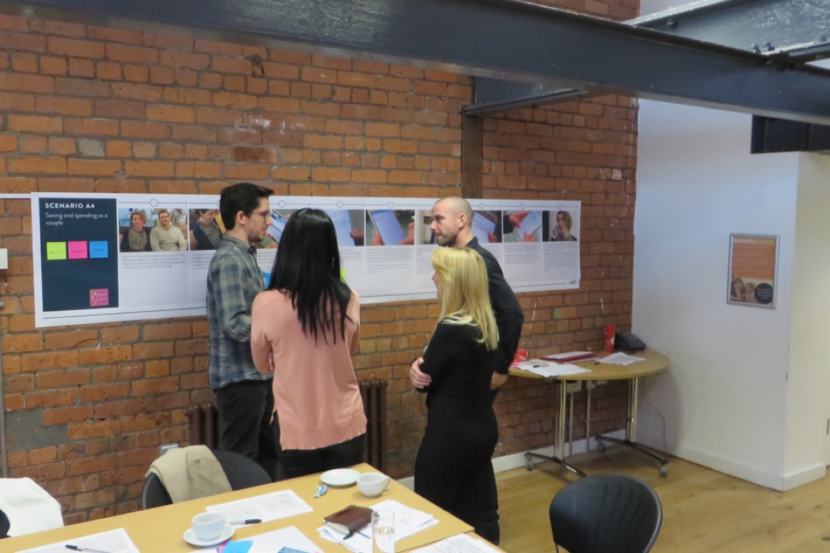 Photograph of a group standing in front of a storyboard discussing app features.