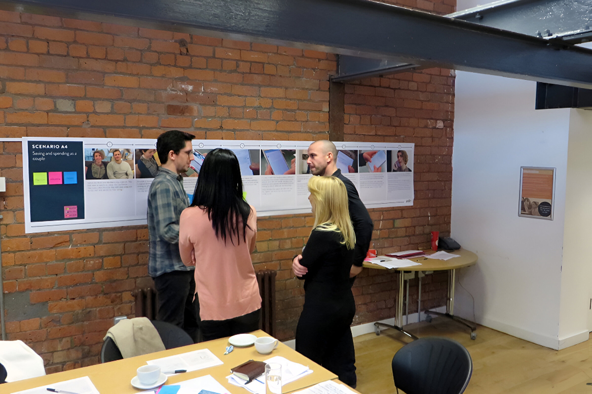Photograph of a group standing in front of a storyboard discussing app features.